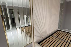 Lustra z fazowanych pasów w złotej ramie ze stali nierdzewnej obok ściennych paneli tapicerowanych